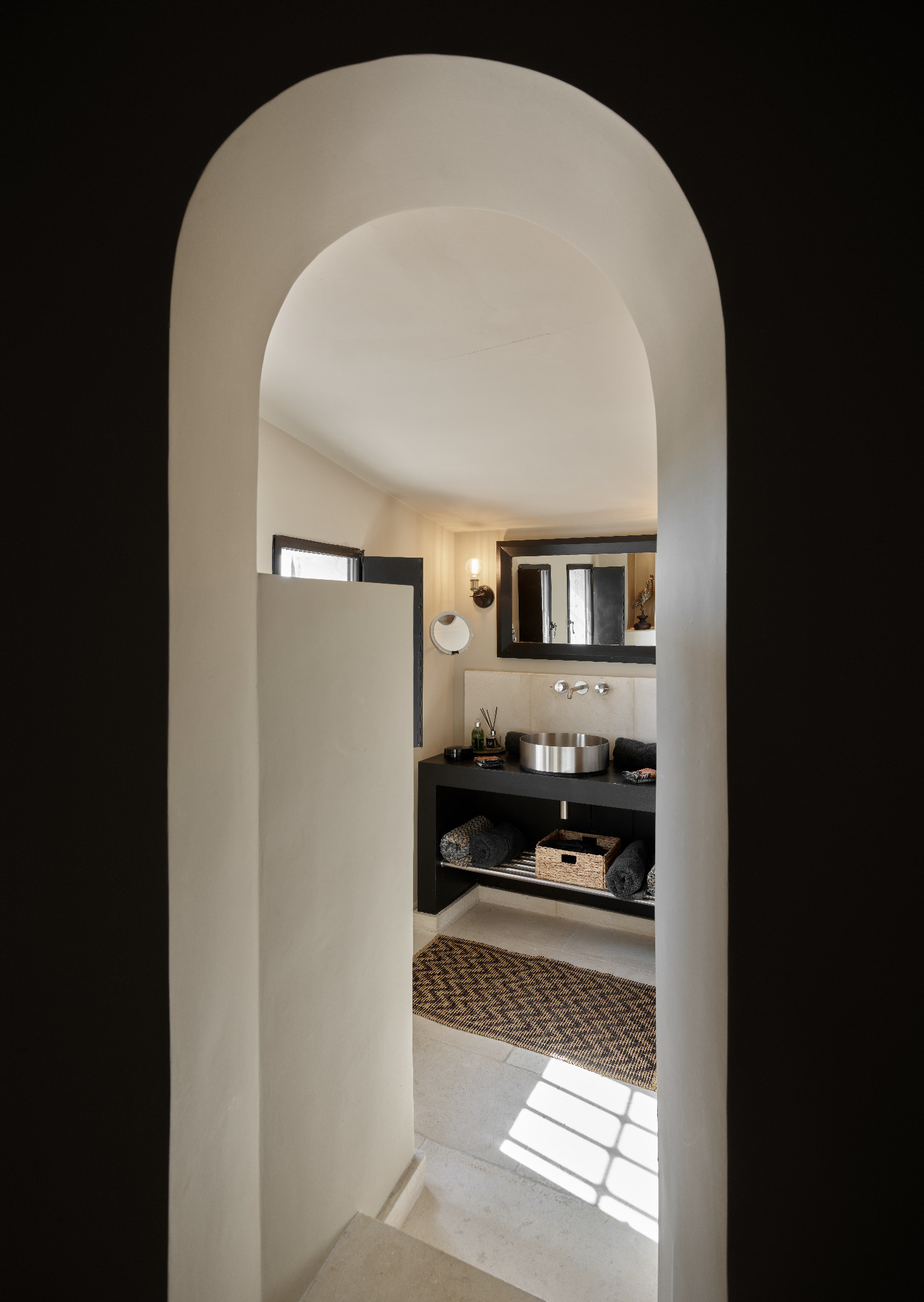 Private bathroom through arched entrance with black vanity and metallic basin